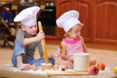İki kardeş - erkek ve kız - şöminenin yanında aşçı şapkası takmış mutfakta un ile kirlenmiş, yemekle oynuyor, ortalığı dağıtıyor ve eğleniyorlar.