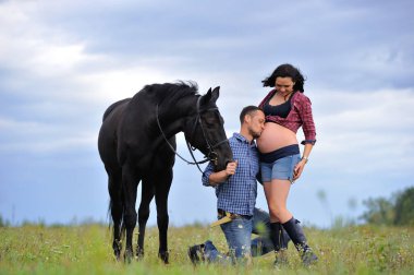 Mutlu çift - uzun saçlı, uzun saçlı, yakışıklı esmer; adam dizlerinin üzerinde, onun göbeğini öpüyor ve siyah atın dizginlerini tutuyor. Meadow, arkasında harika bir gökyüzü