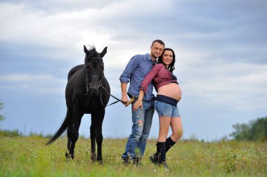 Çocuğunu bekliyor. Genç bir çift - uzun saçlı esmer, hamile; uzun boylu ve cesur, siyah atın dizginlerini tutan, çiftlikte bir yürüyüş.