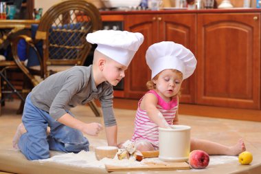 İki kardeş - erkek ve kız - şöminenin yanında aşçı şapkası takmış mutfakta un ile kirlenmiş, yemekle oynuyor, ortalığı dağıtıyor ve eğleniyorlar.