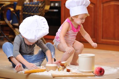 İki kardeş - erkek ve kız - şöminenin yanında aşçı şapkası takmış mutfakta un ile kirlenmiş, yemekle oynuyor, ortalığı dağıtıyor ve eğleniyorlar.