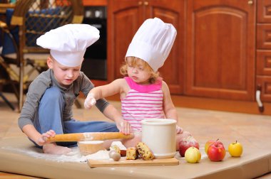 İki kardeş - erkek ve kız - şöminenin yanında aşçı şapkası takmış mutfakta un ile kirlenmiş, yemekle oynuyor, ortalığı dağıtıyor ve eğleniyorlar.