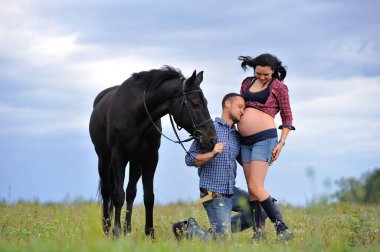 Mutlu çift - uzun saçlı, uzun saçlı, yakışıklı esmer; adam dizlerinin üzerinde, onun göbeğini öpüyor ve siyah atın dizginlerini tutuyor. Meadow, arkasında harika bir gökyüzü