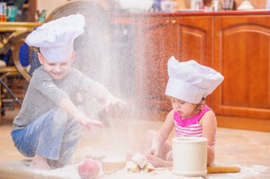 İki kardeş - erkek ve kız - şöminenin yanında aşçı şapkası takmış mutfakta un ile kirlenmiş, yemekle oynuyor, ortalığı dağıtıyor ve eğleniyorlar.