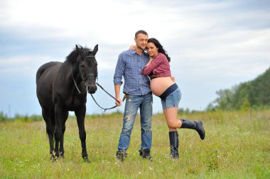 Çocuğunu bekliyor. Genç bir çift - uzun saçlı esmer, hamile; uzun boylu ve cesur, siyah atın dizginlerini tutan, çiftlikte bir yürüyüş.