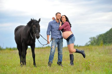 Çocuğunu bekliyor. Genç bir çift - uzun saçlı esmer, hamile; uzun boylu ve cesur, siyah atın dizginlerini tutan, çiftlikte bir yürüyüş.