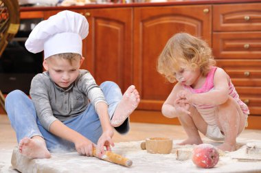 İki kardeş - erkek ve kız - şöminenin yanında aşçı şapkası takmış mutfakta un ile kirlenmiş, yemekle oynuyor, ortalığı dağıtıyor ve eğleniyorlar.