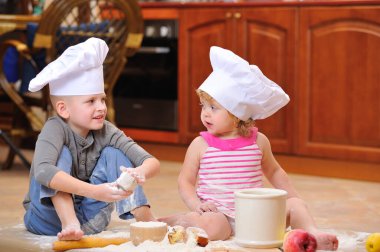 İki kardeş - erkek ve kız - şöminenin yanında aşçı şapkası takmış mutfakta un ile kirlenmiş, yemekle oynuyor, ortalığı dağıtıyor ve eğleniyorlar.