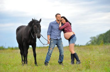 Çocuğunu bekliyor. Genç bir çift - uzun saçlı esmer, hamile; uzun boylu ve cesur, siyah atın dizginlerini tutan, çiftlikte bir yürüyüş.