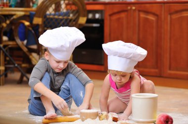 İki kardeş - erkek ve kız - şöminenin yanında aşçı şapkası takmış mutfakta un ile kirlenmiş, yemekle oynuyor, ortalığı dağıtıyor ve eğleniyorlar.