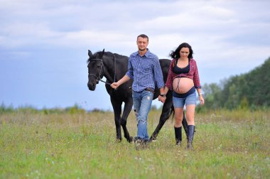 Çocuğunu bekliyor. Genç bir çift - uzun saçlı esmer, hamile; uzun boylu ve cesur, siyah atın dizginlerini tutan, çiftlikte bir yürüyüş.