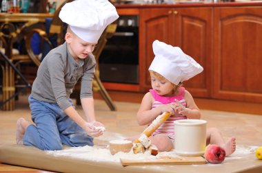 İki kardeş - erkek ve kız - şöminenin yanında aşçı şapkası takmış mutfakta un ile kirlenmiş, yemekle oynuyor, ortalığı dağıtıyor ve eğleniyorlar.