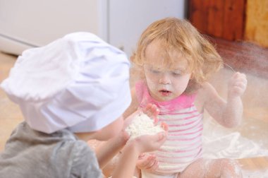 İki kardeş - erkek ve kız - şöminenin yanında aşçı şapkası takmış mutfakta un ile kirlenmiş, yemekle oynuyor, ortalığı dağıtıyor ve eğleniyorlar.