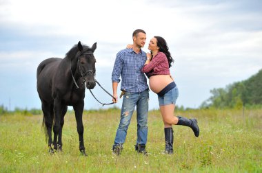 Çocuğunu bekliyor. Genç bir çift - uzun saçlı esmer, hamile; uzun boylu ve cesur, siyah atın dizginlerini tutan, çiftlikte bir yürüyüş.