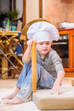 Çocuk mutfakta oturmuş un kirletiyor, yemekle oynuyor, ortalığı dağıtıyor ve eğleniyor.