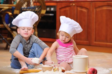 İki kardeş - erkek ve kız - şöminenin yanında aşçı şapkası takmış mutfakta un ile kirlenmiş, yemekle oynuyor, ortalığı dağıtıyor ve eğleniyorlar.