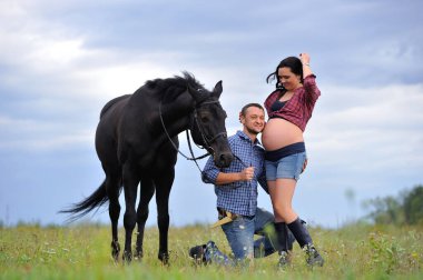 Mutlu çift - uzun saçlı, uzun saçlı, yakışıklı esmer; adam dizlerinin üzerinde, onun göbeğini öpüyor ve siyah atın dizginlerini tutuyor. Meadow, arkasında harika bir gökyüzü