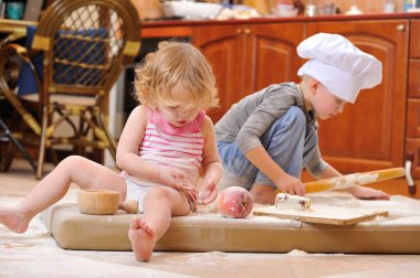 İki kardeş - erkek ve kız - şöminenin yanında aşçı şapkası takmış mutfakta un ile kirlenmiş, yemekle oynuyor, ortalığı dağıtıyor ve eğleniyorlar.