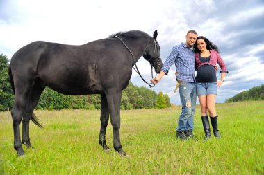 Çocuğunu bekliyor. Genç çift - uzun saçlı, esmer, yakışıklı ve hamile; uzun boylu ve cesur, siyah atın dizginlerini tutan, mavi gökyüzüne karşı çayırda bir yürüyüş