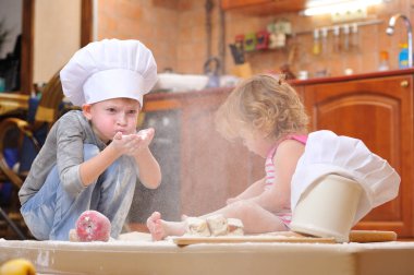 İki kardeş - erkek ve kız - şöminenin yanında aşçı şapkası takmış mutfakta un ile kirlenmiş, yemekle oynuyor, ortalığı dağıtıyor ve eğleniyorlar.