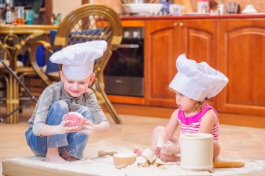 İki kardeş - erkek ve kız - şöminenin yanında aşçı şapkası takmış mutfakta un ile kirlenmiş, yemekle oynuyor, ortalığı dağıtıyor ve eğleniyorlar.