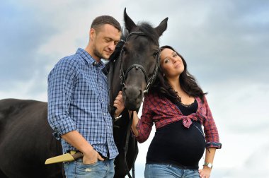 Çocuğunu bekliyor. Genç bir çift - uzun saçlı esmer, hamile; uzun boylu ve cesur, siyah atın dizginlerini tutan, çiftlikte bir yürüyüş.