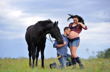 Mutlu çift - uzun saçlı, uzun saçlı, yakışıklı esmer; adam dizlerinin üzerinde, onun göbeğini öpüyor ve siyah atın dizginlerini tutuyor. Meadow, arkasında harika bir gökyüzü