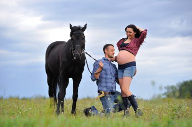 Mutlu çift - uzun saçlı, uzun saçlı, yakışıklı esmer; adam dizlerinin üzerinde, onun göbeğini öpüyor ve siyah atın dizginlerini tutuyor. Meadow, arkasında harika bir gökyüzü