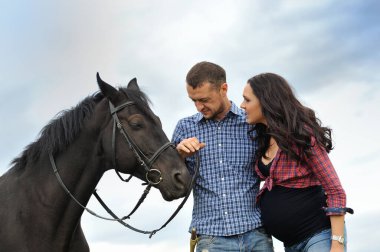 Çiftlikte bir yürüyüş. Genç bir çift - o uzun saçlı, hamile bir esmer; uzun boylu ve cesur, siyah atın dizginlerini tutan