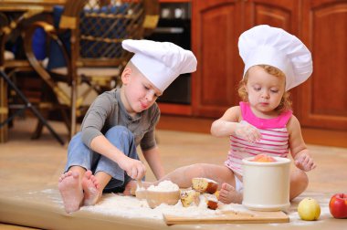 İki kardeş - erkek ve kız - şöminenin yanında aşçı şapkası takmış mutfakta un ile kirlenmiş, yemekle oynuyor, ortalığı dağıtıyor ve eğleniyorlar.