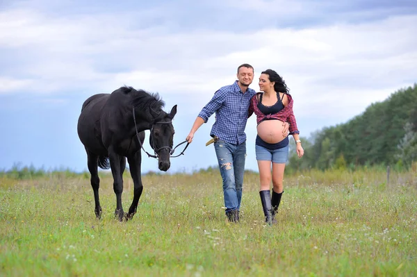 Çocuğunu bekliyor. Genç bir çift - uzun saçlı esmer, hamile; uzun boylu ve cesur, siyah atın dizginlerini tutan, çiftlikte bir yürüyüş.