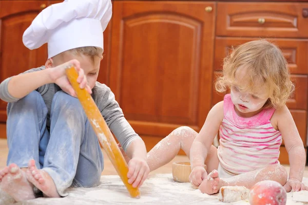 İki kardeş - erkek ve kız - şöminenin yanında aşçı şapkası takmış mutfakta un ile kirlenmiş, yemekle oynuyor, ortalığı dağıtıyor ve eğleniyorlar.