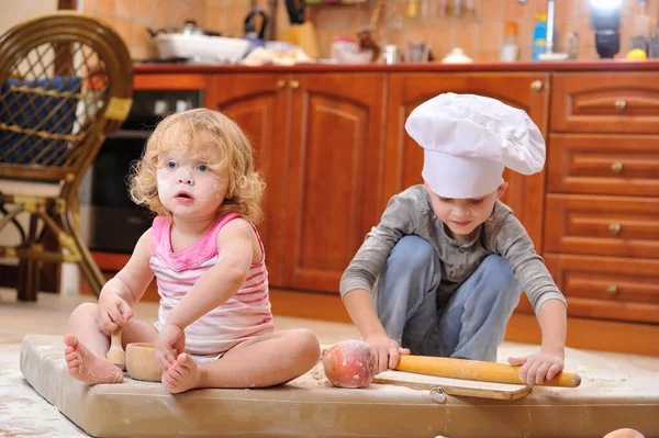 两个兄弟姐妹 男孩和女孩 戴着厨师帽 坐在厨房地板上 沾满了面粉 玩着食物 弄得乱七八糟 玩得很开心 — 图库照片