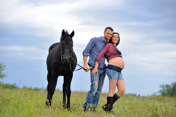 Çocuğunu bekliyor. Genç bir çift - uzun saçlı esmer, hamile; uzun boylu ve cesur, siyah atın dizginlerini tutan, çiftlikte bir yürüyüş.