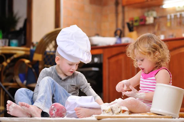İki kardeş - erkek ve kız - şöminenin yanında aşçı şapkası takmış mutfakta un ile kirlenmiş, yemekle oynuyor, ortalığı dağıtıyor ve eğleniyorlar.