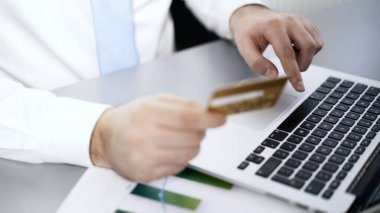 Kredi kartlı bir adam dizüstü bilgisayarda yazıyor, menajer online alışveriş yapıyor, yüzü yok.