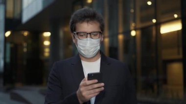 Akşam maskeli bir adam cam pencerelerin arkasında telefonu kaydırıyor.
