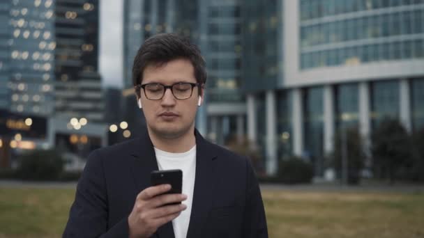 Мужчина в костюме стоит с телефоном на фоне бизнес-центра — стоковое видео