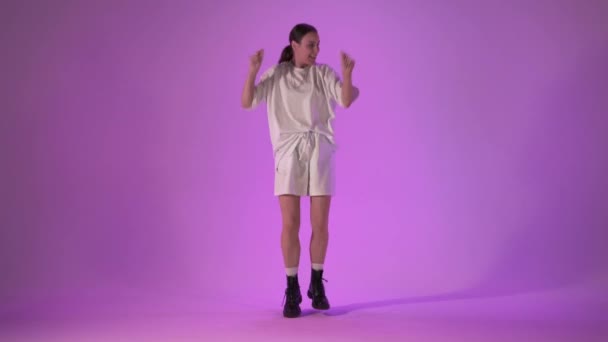 Jeune femme dansant hip hop sur fond violet, plan studio — Video