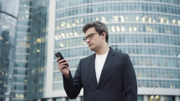 Человек, стоящий с телефоном на фоне бизнес-центра — стоковое видео