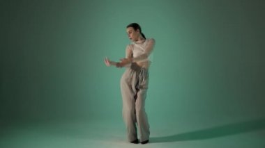 Yeşil arka planda beyaz spor kıyafetlerle dans eden kız, stüdyo çekimi.