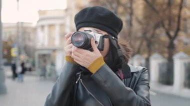 Bereli genç bir kadın dışarıda fotoğraf makinesiyle ateş ediyor, sonbahar rüzgarlı bir günde.