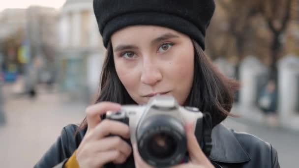 Mujer joven en boina de tiro con una cámara de fotos mirando directamente a la cámara — Vídeos de Stock