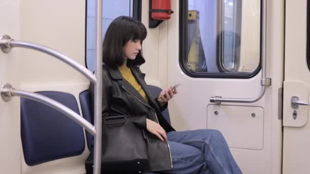 Mujer joven usando el teléfono en un asiento dentro del vagón de metro, viajando bajo tierra — Vídeo de stock