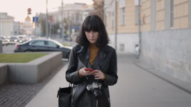 Женщина с фотокамерой с помощью смартфона прогуливается по городской улице — стоковое видео