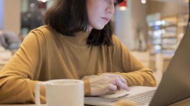 Kafede dizüstü bilgisayarı olan genç Asyalı bir kadın, masada bir fincan kahveyle.