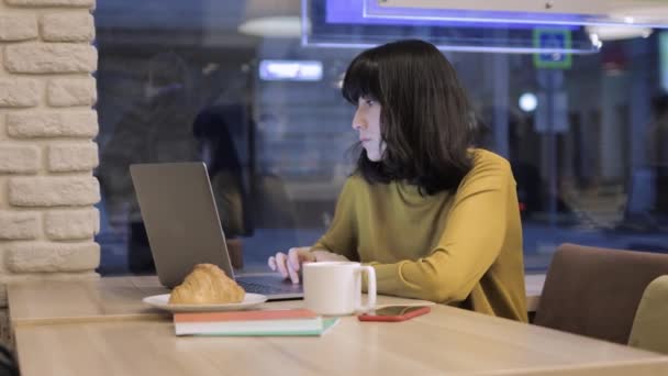 年轻的亚洲女人，带着笔记本电脑，咖啡和羊角面包放在桌上 — 图库视频影像