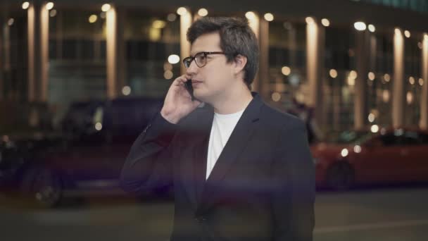 Бізнесмен в окулярах з телефоном говорить на фоні будівлі — стокове відео