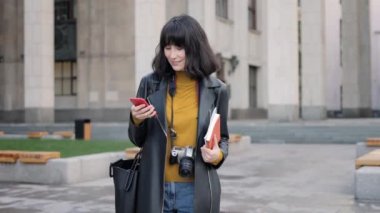 Fotoğraf makineli bir kadın büyük bir binanın arka planında akıllı telefon kullanıyor.