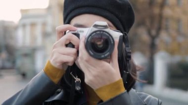 Bere giymiş genç bir kadın fotoğraf makinesiyle kameraya bakıyor.